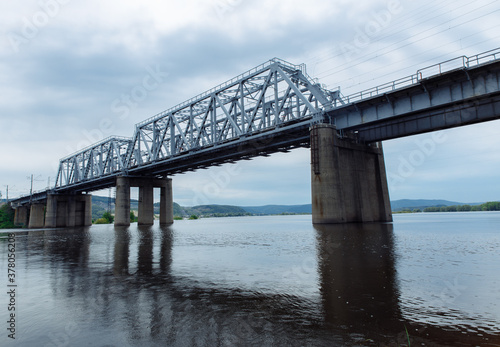 Railway bridge over the river against a cloudy sky. The bridge is reflected in the muddy water. High quality photo