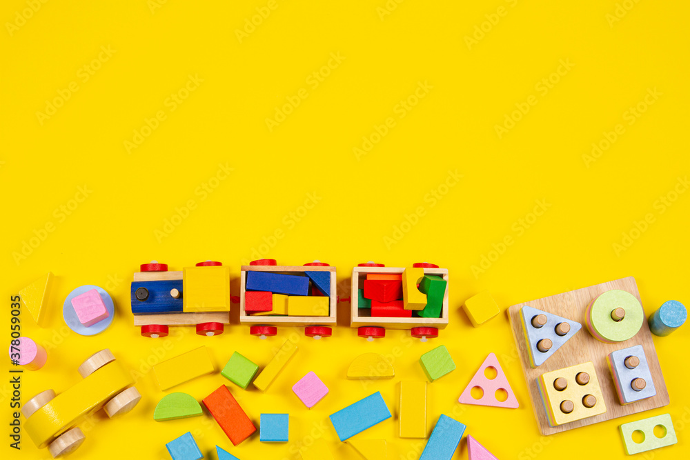 Baby kids toys background. Wooden train, educational stacking color recognition puzzle toy and colorful blocks on yellow background. Top view