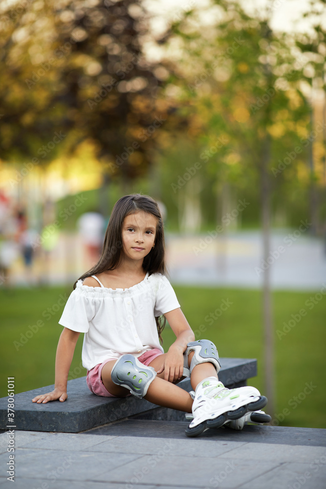 happy little child girl in roller skates is sitting in summer park. happy little child girl in roller skates is sitting in summer park.