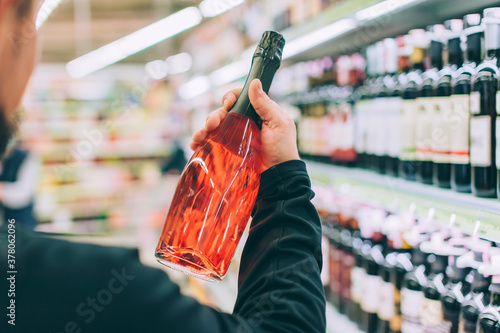 The guy is holding a bottle of wine in the store.