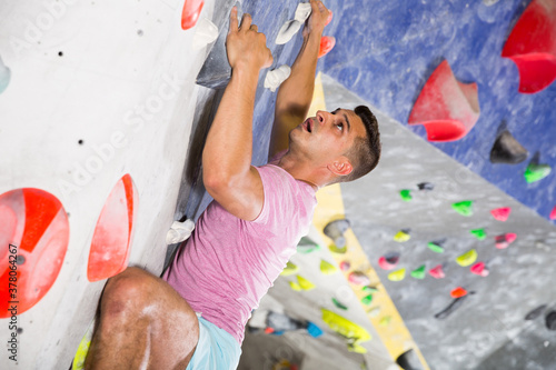 Male alpinist practicing indoor rock-climbing on artificial boulder without safety belts..