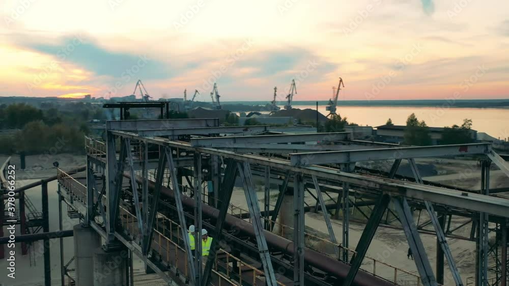 Industrial construction in the port with two engineers walking along it Industrial construction in the port with two engineers walking along it