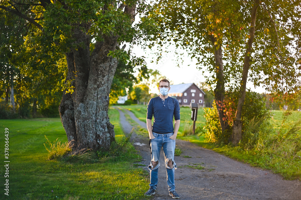 portrait of attractive nerd in long sleeve glasses and protective face mask outside in the park  at sunset