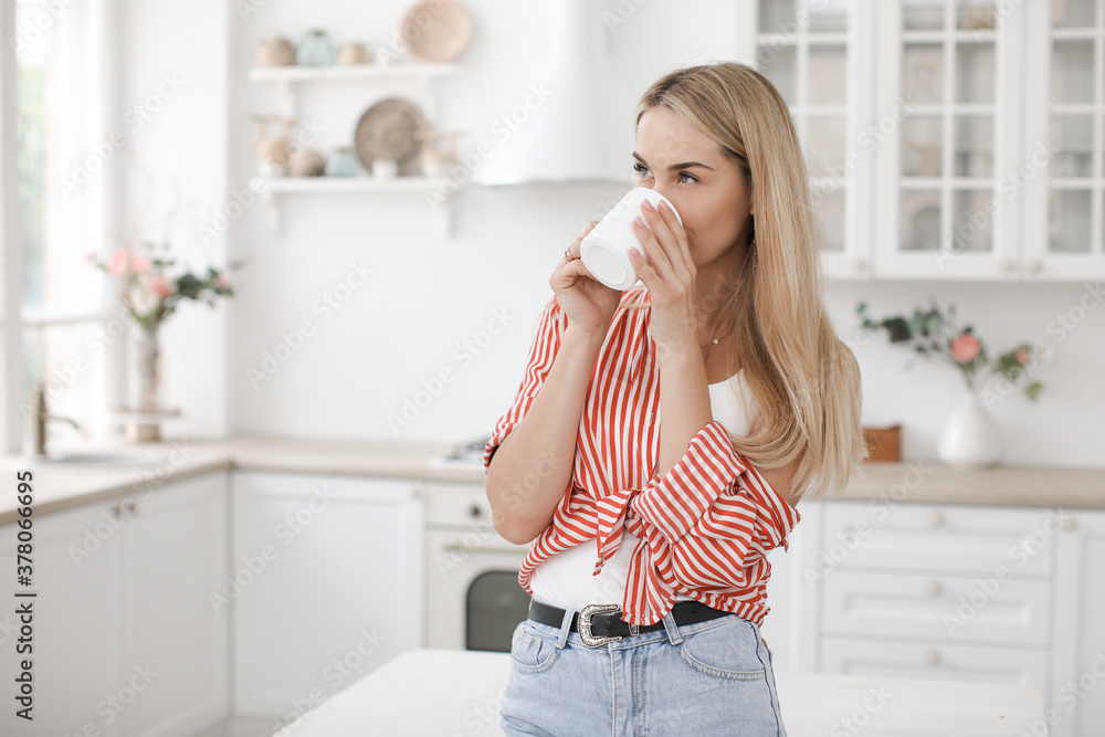 Happy young beautiful woman with cup at home in kitchen