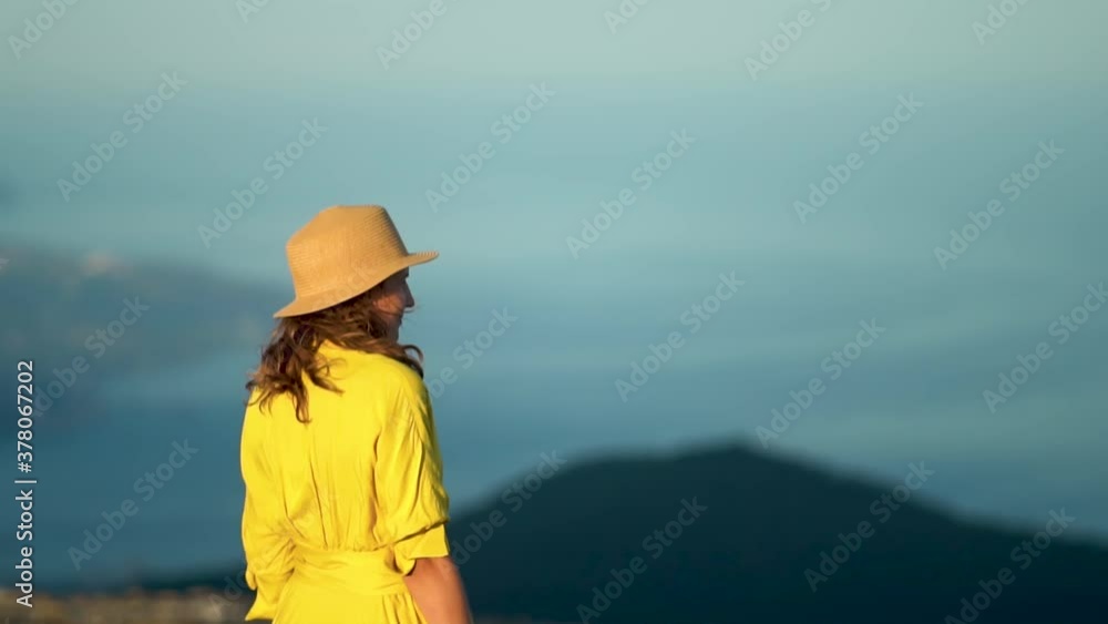 Beautiful young woman in a yellow dress is standing on a cliff of a mountain. The dress and hair flutter in the wind. Travel consept. Slow motion. Beautiful young woman in a yellow dress is standing on a cliff of a mountain. The dress and hair flutter in the wind. Travel consept. Slow motion.