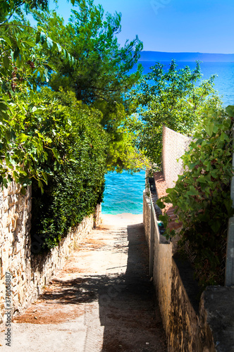 Widok ma lazurowe morze Adriatyckie, wąska dróżka prowadząca na plażę wśród śródziemnomorskiej roślinności © Magdalena