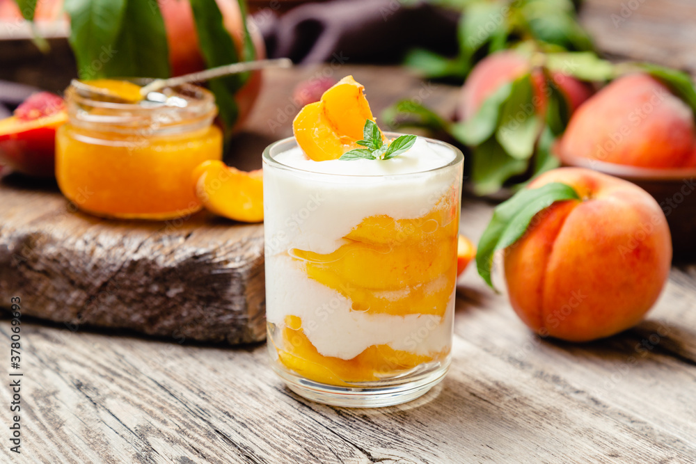 Peach fruit dessert in glass cup on rustic wooden table with fresh peach fruit, peach jam. Homemade dessert with fruits. Fruit salad with yogurt or sour cream. Peach fruit dessert in glass cup on rustic wooden table with fresh peach fruit, peach jam. Homemade dessert with fruits. Fruit salad with yogurt or sour cream.