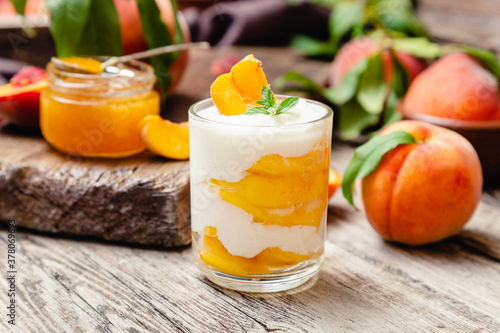 Peach fruit dessert in glass cup on rustic wooden table with fresh peach fruit, peach jam. Homemade dessert with fruits. Fruit salad with yogurt or sour cream.