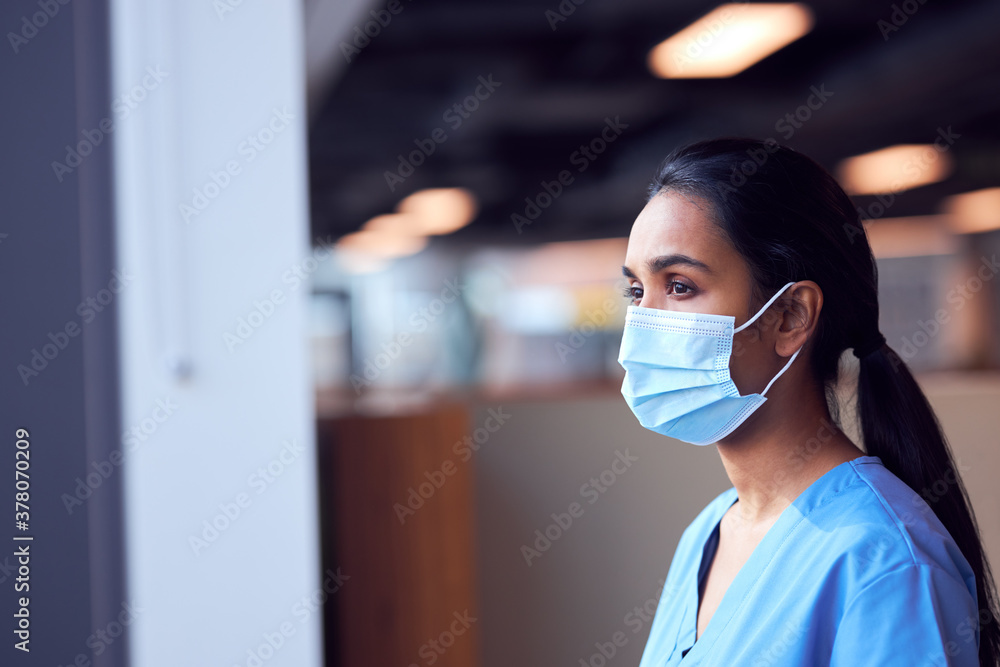 Female Doctor In Face Mask Wearing Scrubs Under Pressure In Busy Hospital During Health Pandemic Female Doctor In Face Mask Wearing Scrubs Under Pressure In Busy Hospital During Health Pandemic