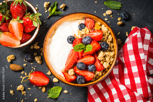Greek yogurt granola with fresh berries on black stone table.