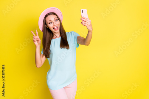 Photo of positive cheerful girl enjoy travel trip take selfie smart phone make v-sign wear blue pink t-shirt pants trousers sunhat isolated over bright shine color background © deagreez