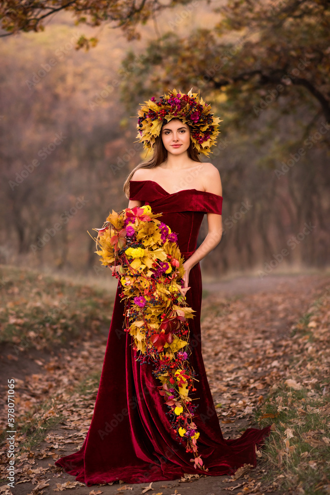 Beautiful young woman in an autumn park in a long dress. Girl with an autumn bouquet in her hands. The woman has a wreath of flowers on her head. Autumn floristry
