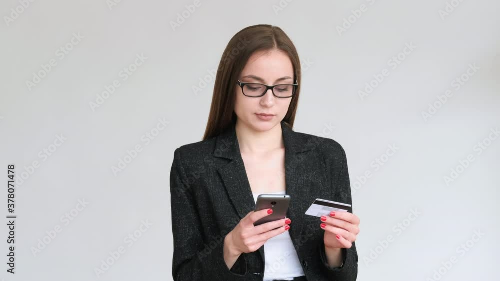 Bank call. Data verification. Confident business woman in glasses black blazer using mobile phone credit card isolated on gray copy space background. Customer support. Cashless payment. Bank call. Data verification. Confident business woman in glasses black blazer using mobile phone credit card isolated on gray copy space background. Customer support. Cashless payment.