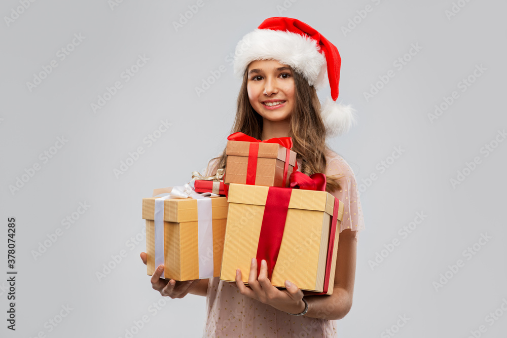 christmas, holidays and people concept - happy smiling teenage girl in santa helper hat holding gift box over grey background christmas, holidays and people concept - happy smiling teenage girl in santa helper hat holding gift box over grey background