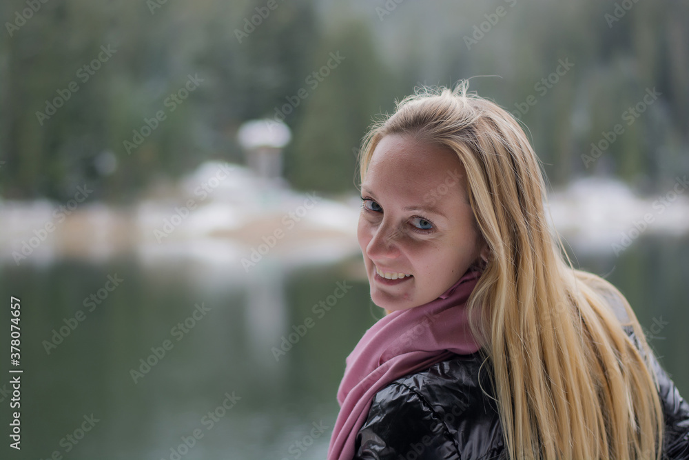A young woman stands by a winter lake. Girl with long blond hair in winter
