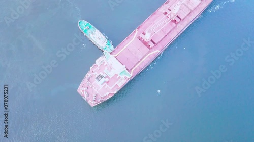 two tugs are doing work on mooring a large cargo ship for loading grain at the seaport berth. The ship is sailing on the calm blue sea on a sunny summer day. aerial view bird's-eye view. drone. quadco photo