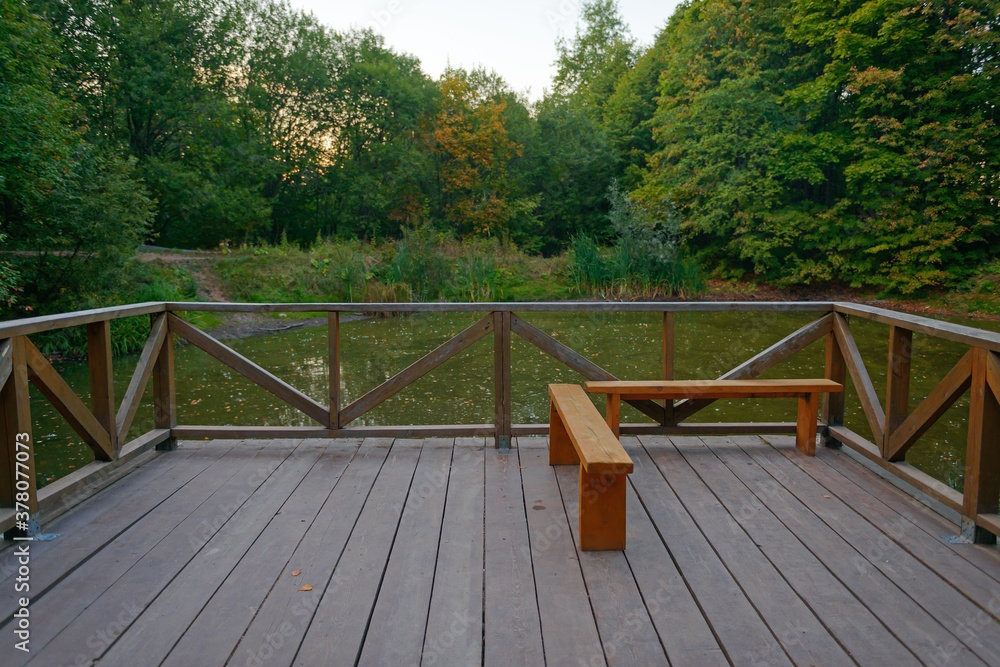 patio with a fence and a bench overlooking a small pond on a summer evening patio with a fence and a bench overlooking a small pond on a summer evening
