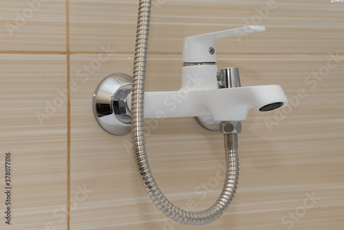 white mixer with hose on the wall of beige tiles