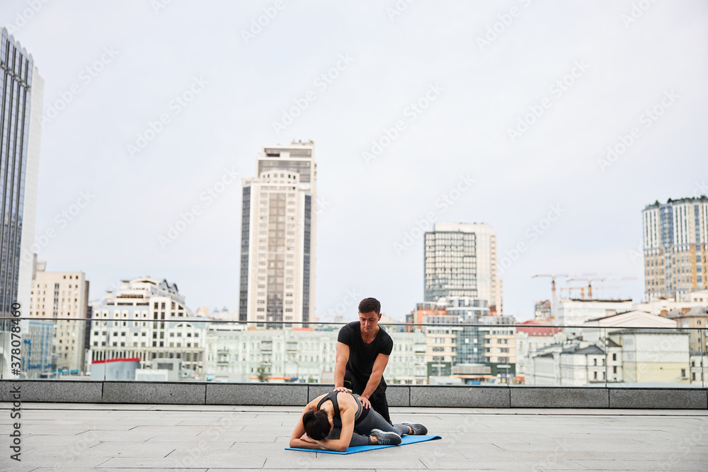 Athletic man training young woman on roof