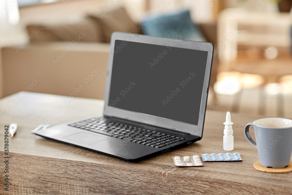 healthcare, technology and medicine concept - laptop computer, drugs and cup on table at home healthcare, technology and medicine concept - laptop computer, drugs and cup on table at home