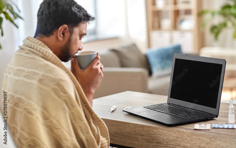 health, cold and people concept - sick young indian man in blanket with laptop computer drinking hot tea and having video call at home health, cold and people concept - sick young indian man in blanket with laptop computer drinking hot tea and having video call at home
