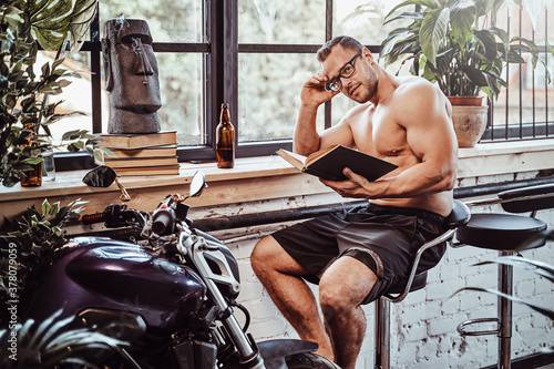 Sportsman with glasses learning and resting in unusal hotel room with plants motorbike and some other stuffs in it.