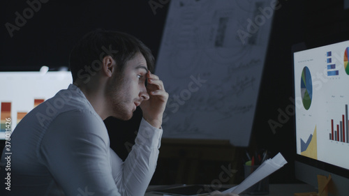 Angry business man throwing document paper on computer table in dark office