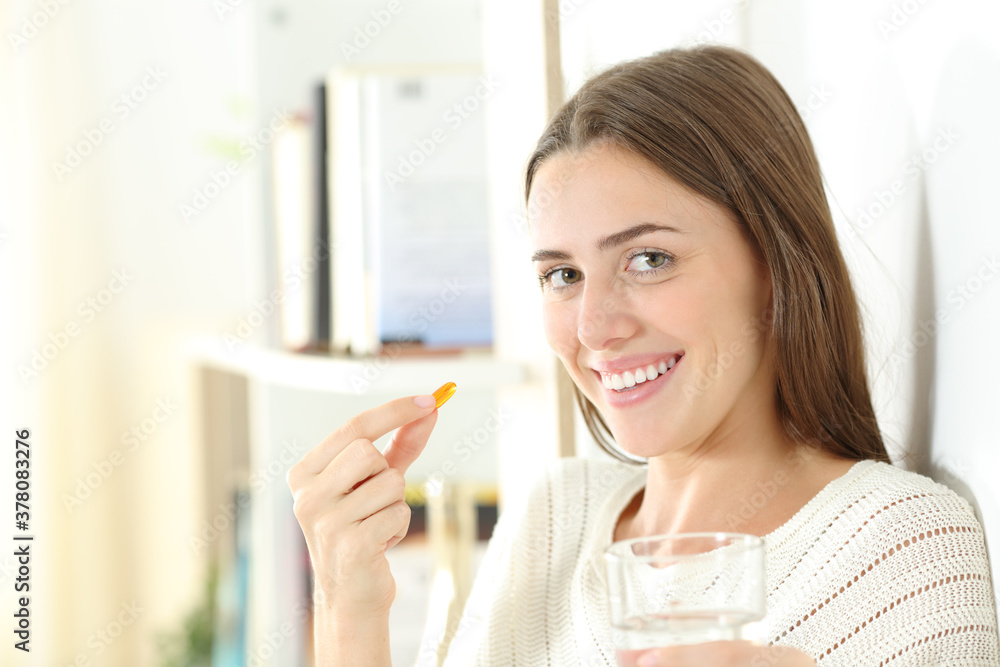 Happy woman holding a vitamin pill ready to eat it Happy woman holding a vitamin pill ready to eat it