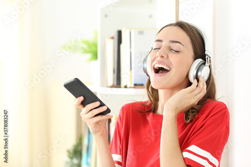 Happy teen singing listening to music on phone at home
