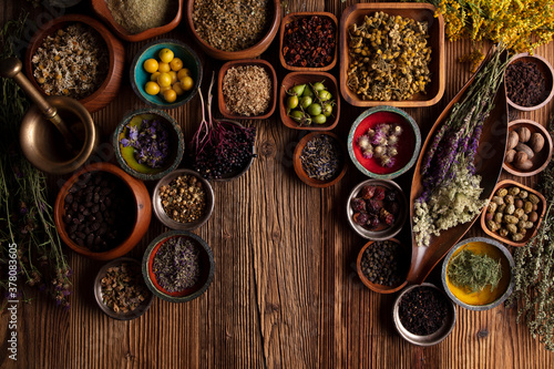 Natural medicine background. Assorted dry herbs in bowls and brass mortar on rustic wooden table.