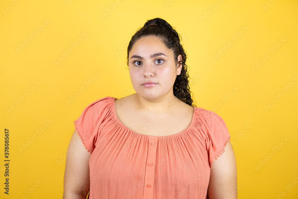Obraz premium Young beautiful woman with curly hair over isolated yellow background serious looking at the camera