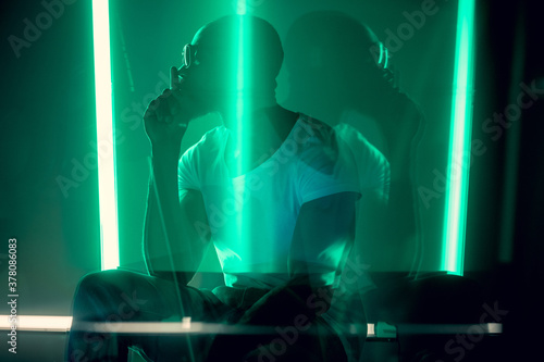 Hip-hop. Cinematic portrait of stylish young man in neon lighted room. Bright neoned colors. African-american model, musician indoors. Youth culture in party, festival style and music concept. © master1305