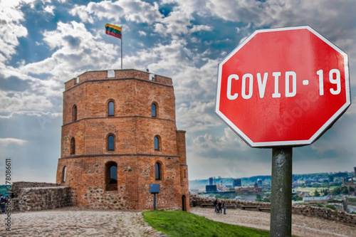 COVID-19 sign against view of Gedeminas tower in Vilnius city center, Lithuania. Warning about pandemic in Lithuania. Coronavirus disease. COVID-19 alert sign