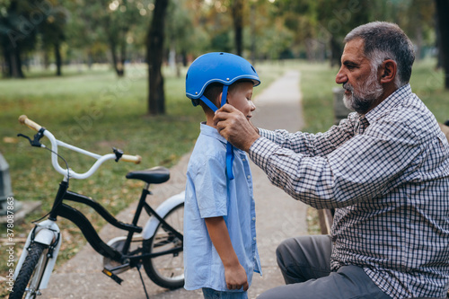 grandfather puts bicycle helmet to his grandson