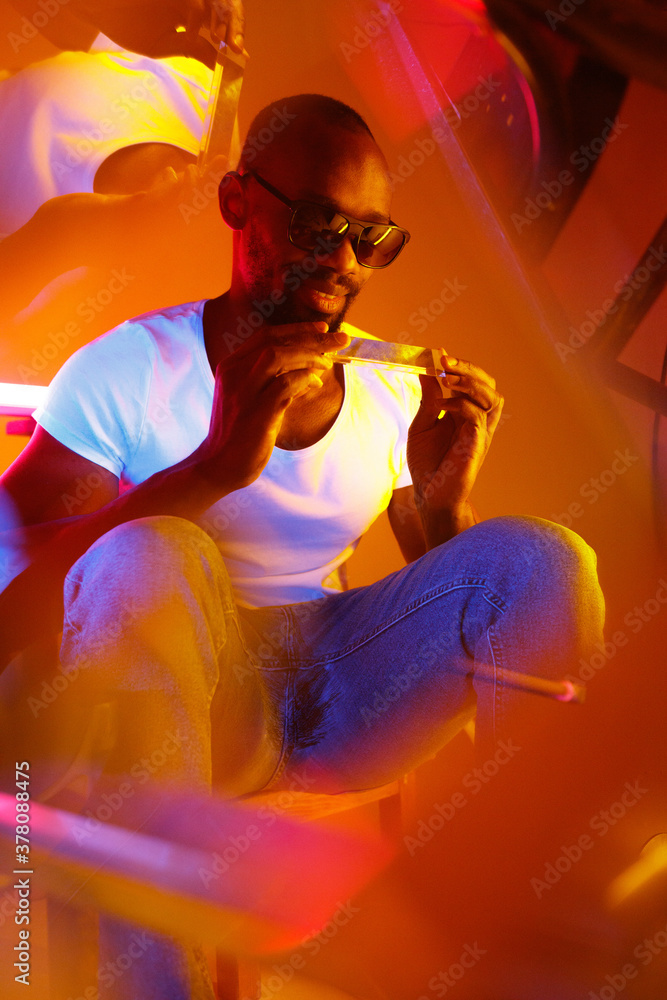 Classy. Cinematic portrait of stylish young man in neon lighted room. Bright neoned colors. African-american model, musician indoors. Youth culture in party, festival style and music concept. Classy. Cinematic portrait of stylish young man in neon lighted room. Bright neoned colors. African-american model, musician indoors. Youth culture in party, festival style and music concept.