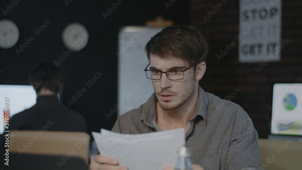 Concentrated business man working with document paper near laptop in dark office Concentrated business man working with document paper near laptop in dark office