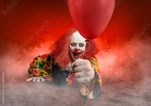 scary clown with a balloon is rising from the sewer