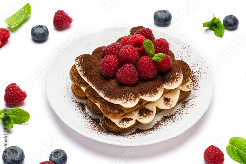 portion of Classic tiramisu dessert with raspberries and blueberries on ceramic plate isolated on white