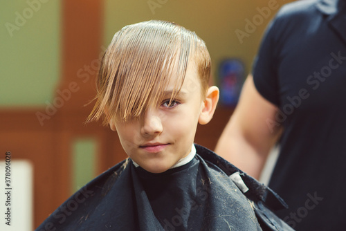 Cute little boy getting haircut by hairdresser at the barbershop. Barber man doing kid the hairstyle.