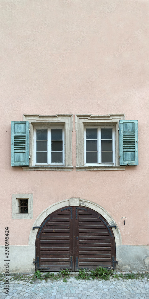 Altes Holztor darüber schöne alte Fenster umrahmt von grünen Fensterläden, rosa Hausfassade, Straße - Pflasterstein,  