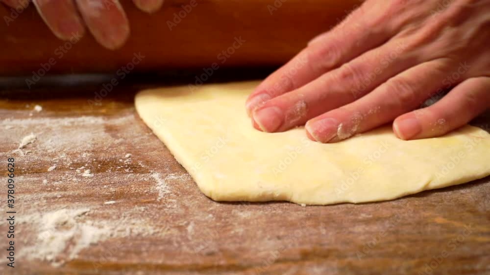 hands roll out a sheet of dough with a rolling pin on a wooden table. hands roll out a sheet of dough with a rolling pin on a wooden table.