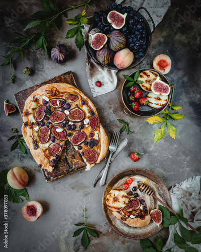 fig and grape pie on wooden board with one slice cut with fresh seasonal fruits and leaves, top view, seasonal dessert 