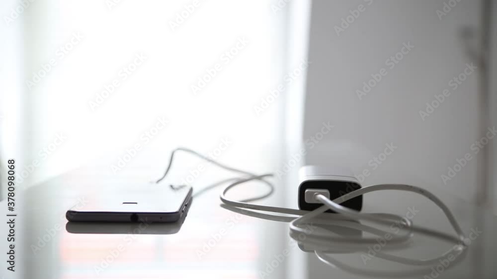 Smartphone is being charged via cable from charger on glass office table Smartphone is being charged via cable from charger on glass office table