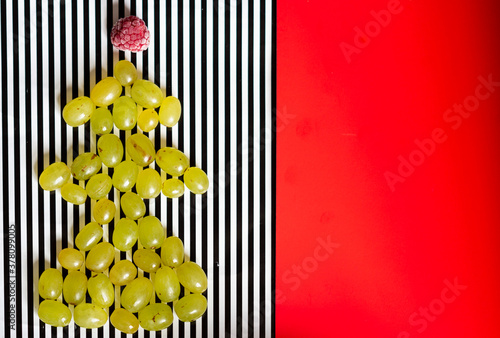 Christmas new year fir eve tree made from green grapes and raspberry on top on black and white with red background