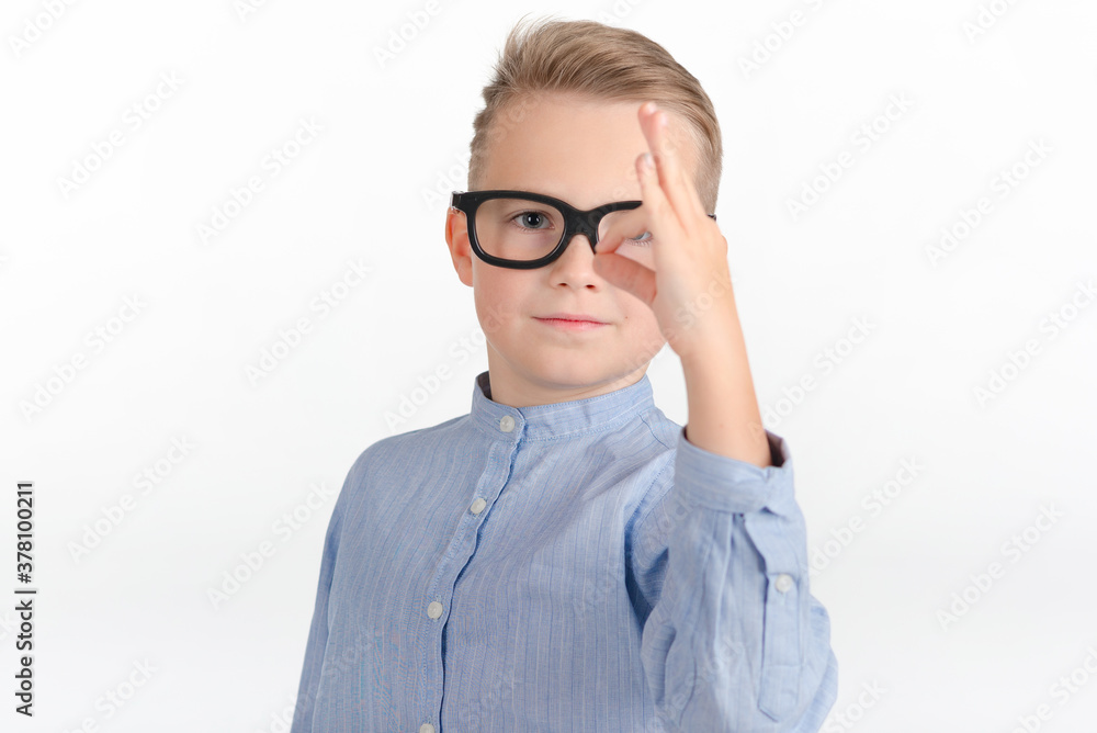 Cute caucasian boy with eyeglasses in blue shirt shows gesture ok or zero.Photo studio white wall. Cute caucasian boy with eyeglasses in blue shirt shows gesture ok or zero.Photo studio white wall.