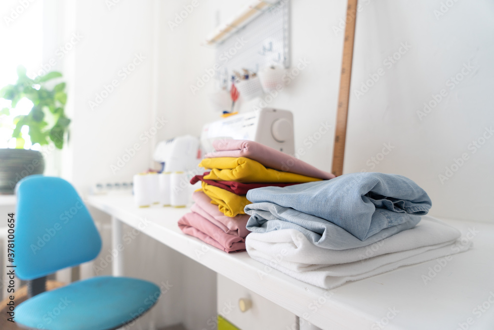Sewing: Several multi-colored canvases of fabrics are stacked and lie on the work table of a tailor. Sewing: Several multi-colored canvases of fabrics are stacked and lie on the work table of a tailor.
