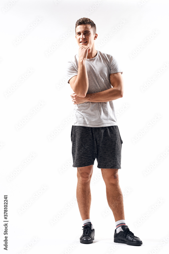 A sports man in shorts and a full-length T-shirt does exercises on a light background A sports man in shorts and a full-length T-shirt does exercises on a light background