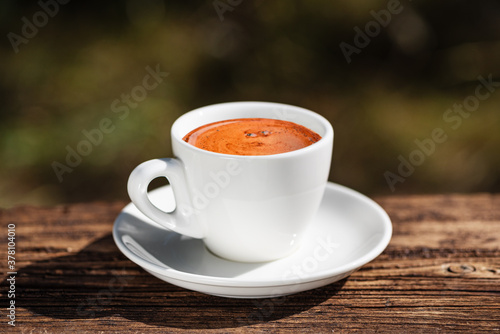 White cup of coffee on wooden table on blurred background. Beautiful golden foam. Coffee time. Copy space.