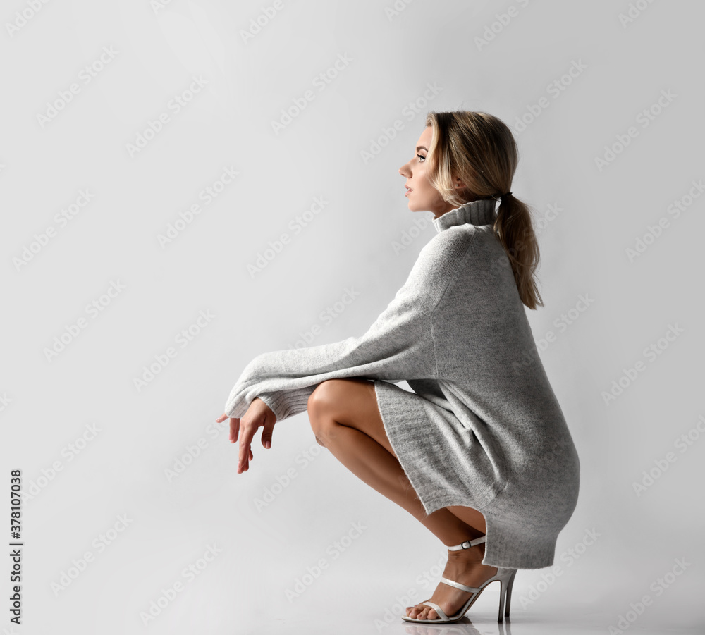 Young sexy beautiful woman in warm knitted sweater and high heels shoes sitting on floor and looking ahead