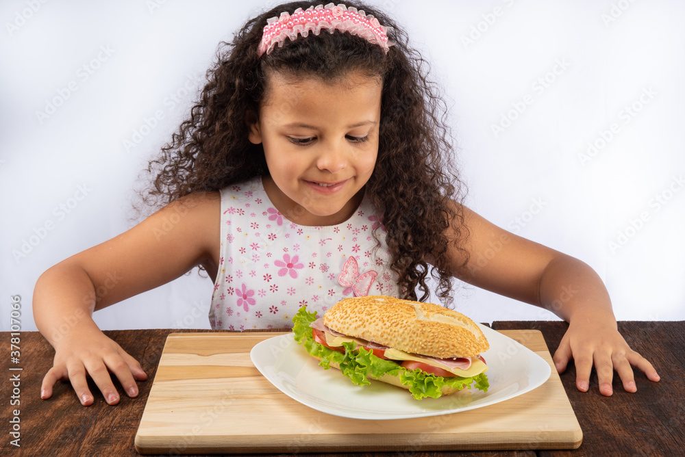 Beautiful child wanting a sandwich that is on a white plate on wood on a rustic wooden table, selective focus.